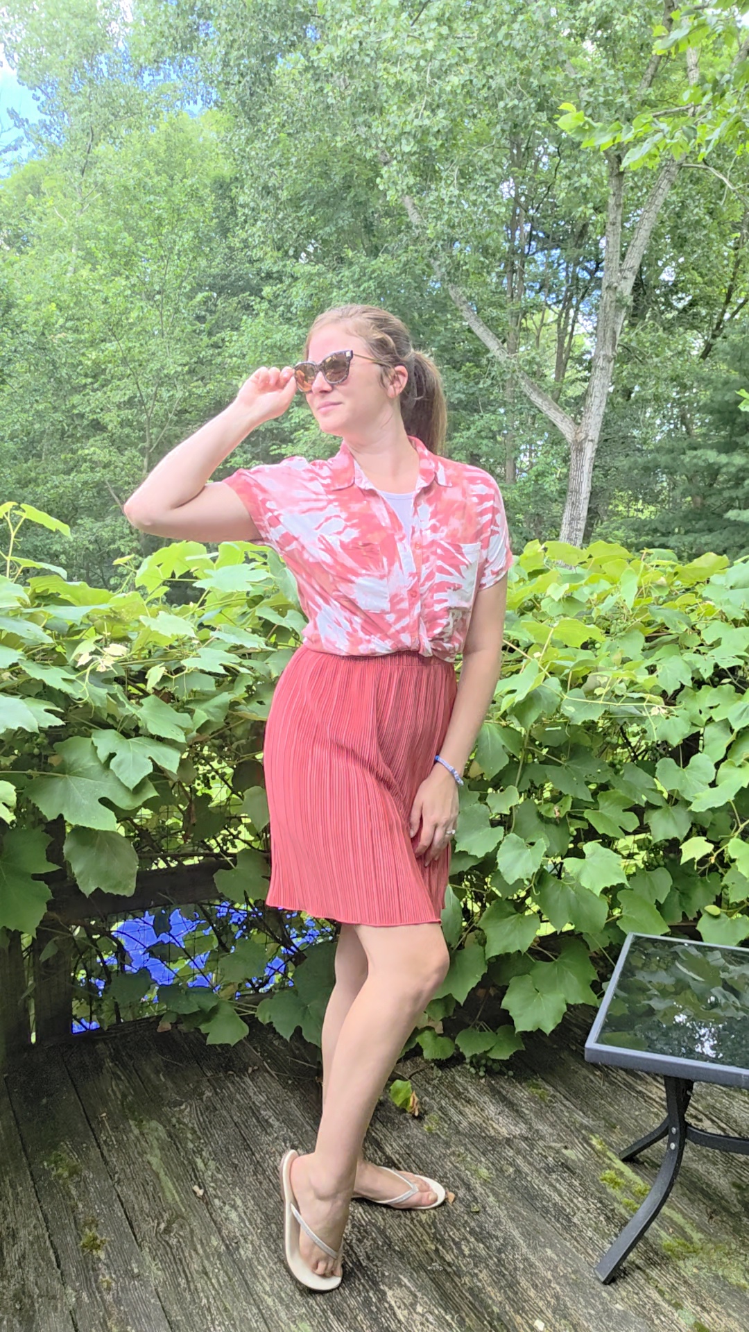 Courtney wearing a pink patterned blouse and pleated skirt in a garden
