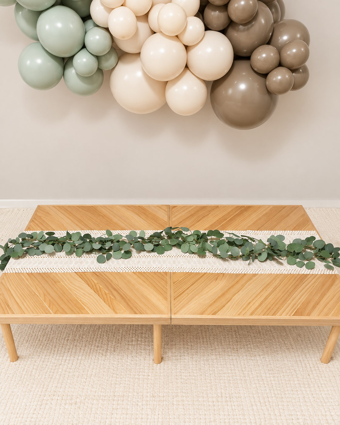 Low wooden party table with a soft greenery runner and neutral balloon garland