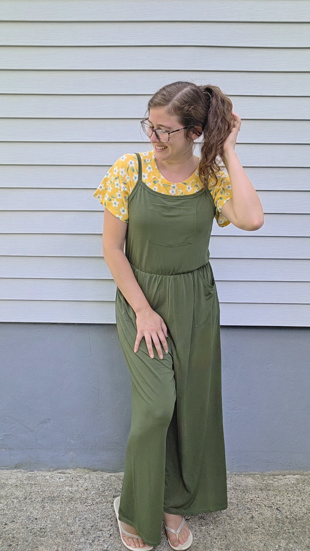 Courtney wearing a green utility jumpsuit layered over a yellow floral top