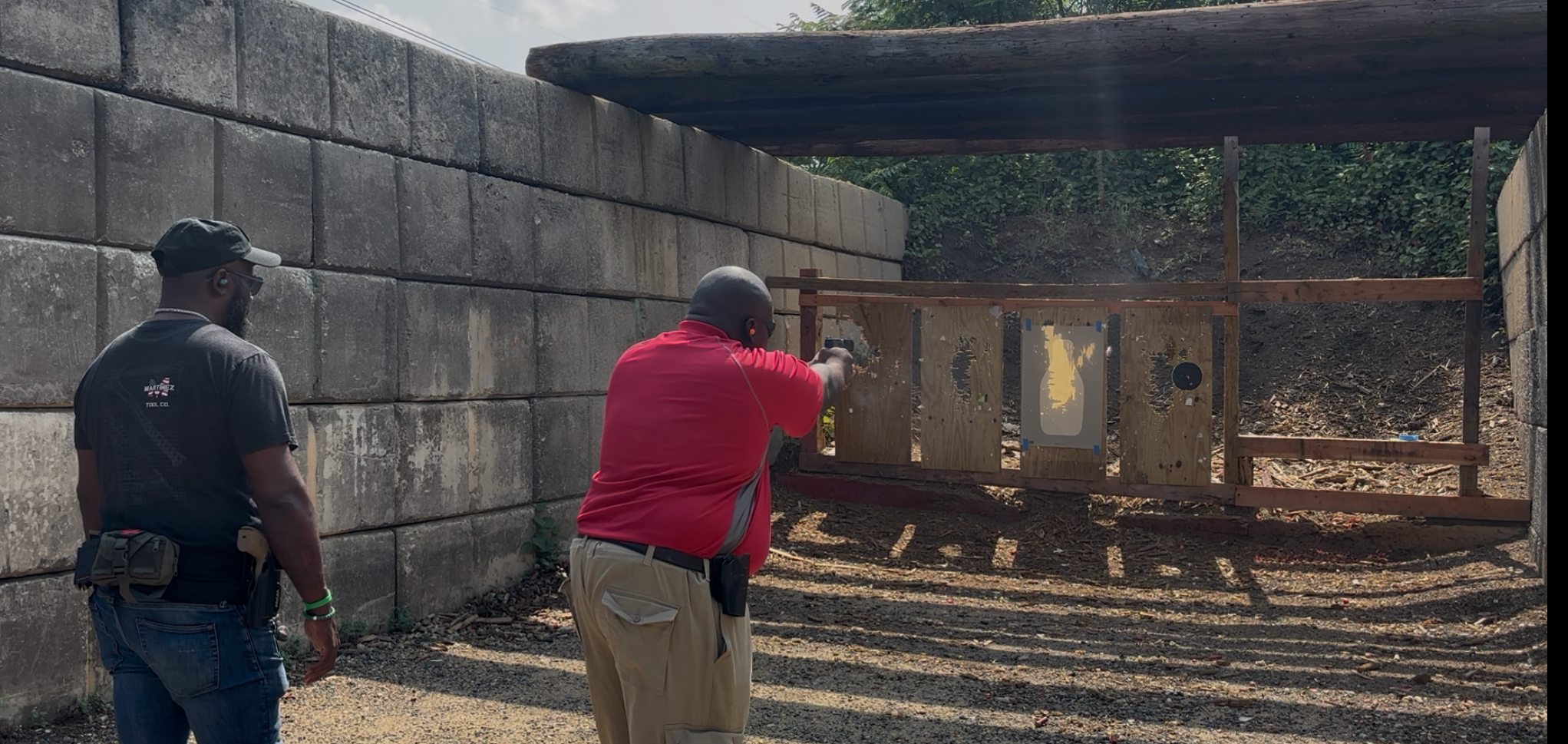 An instructor observes a student practicing at an outdoor shooting range.