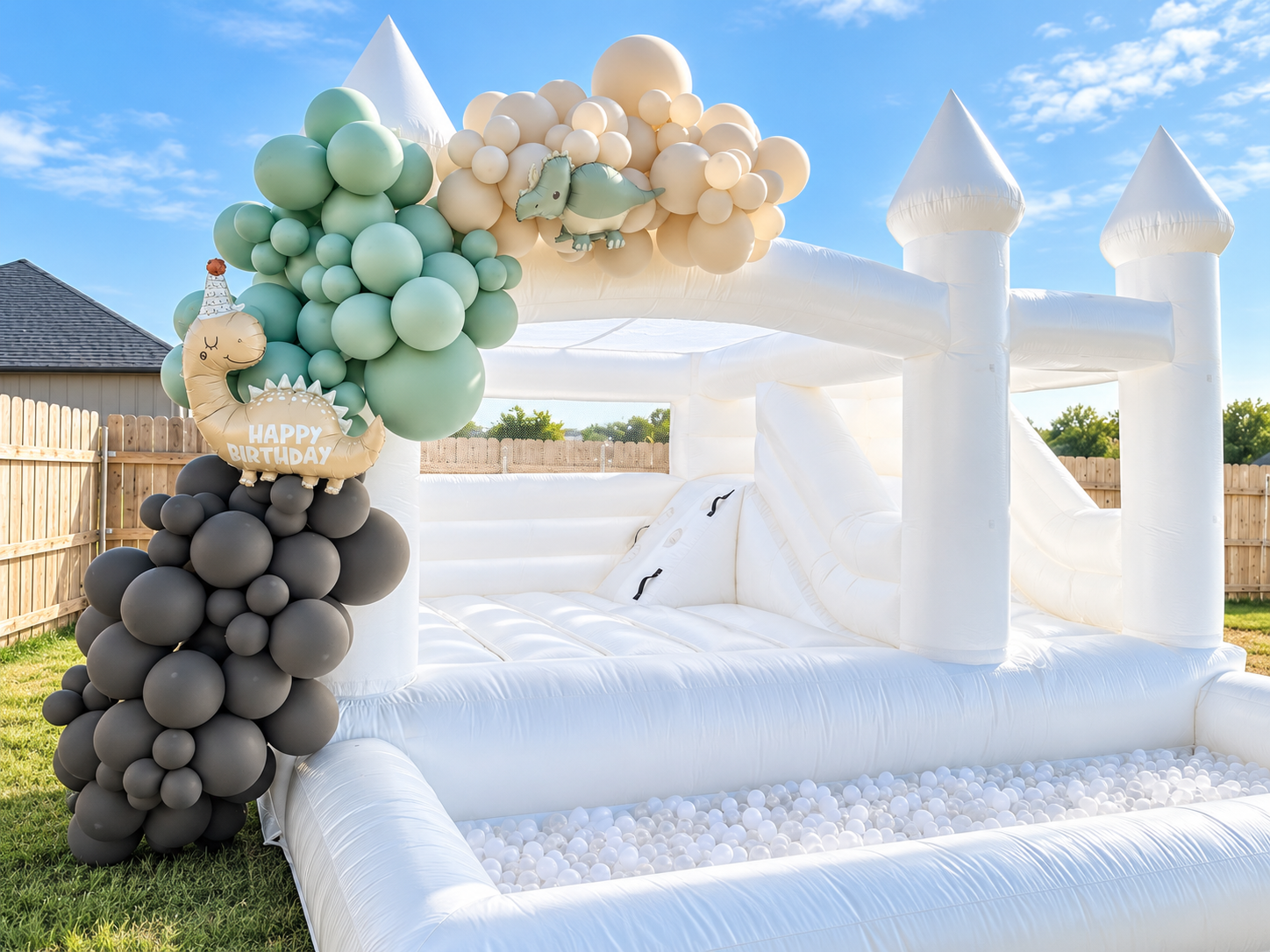 White bounce house with a dinosaur balloon display and ball pit