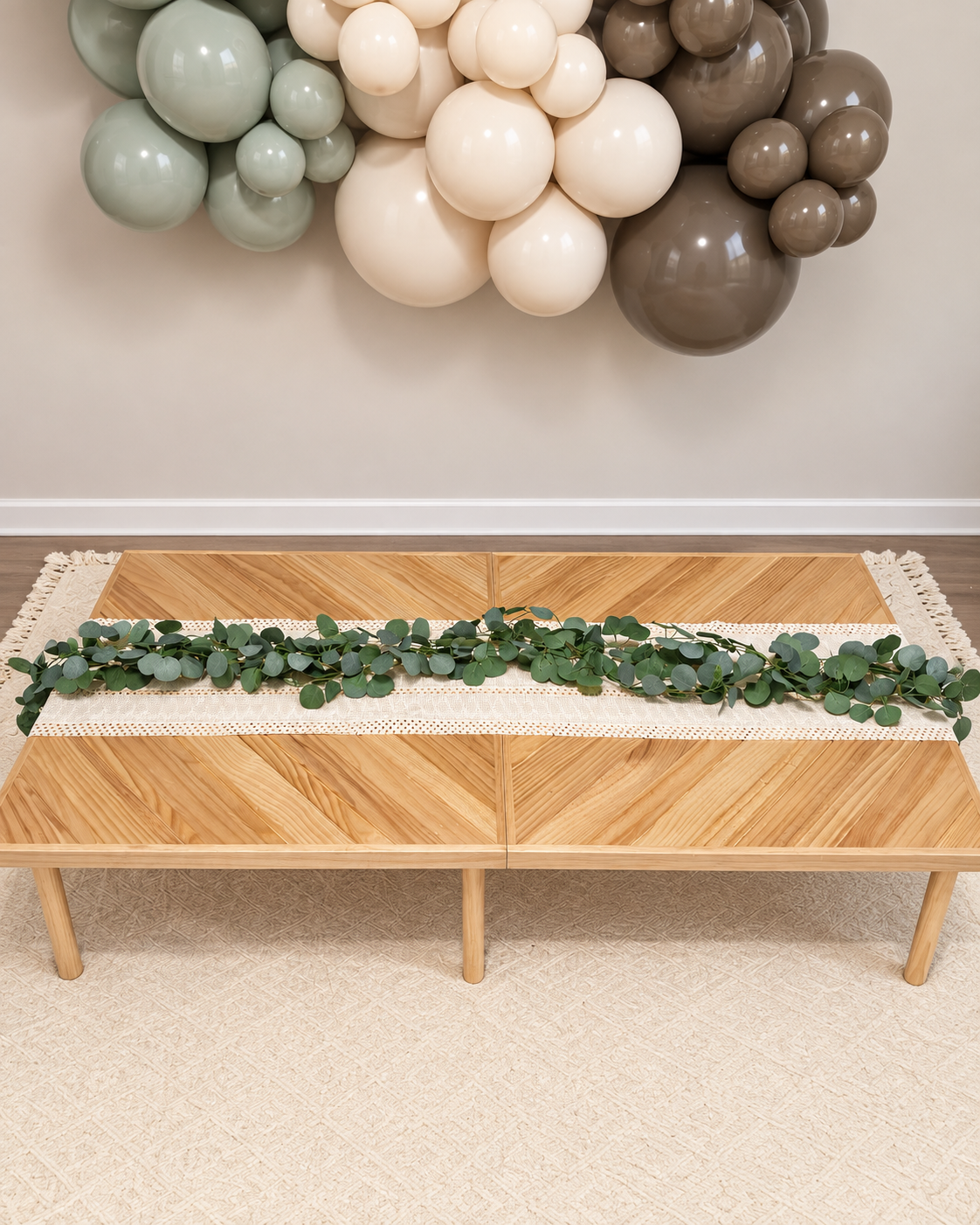 Low wooden party table with a greenery runner and neutral balloon garland