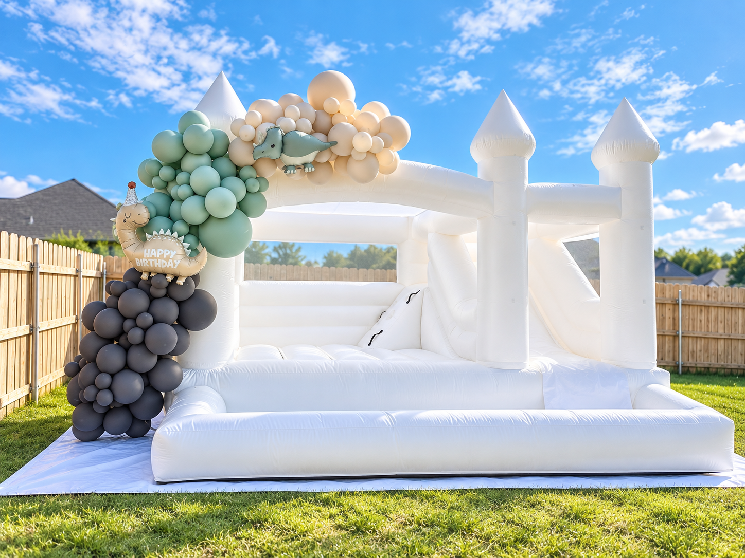 White bounce house with a playful dinosaur balloon garland outdoors